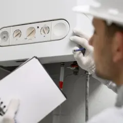 Instalator w białej rękawiczce sprawdza piec gazowy, notując szczegóły dotyczące montażu.