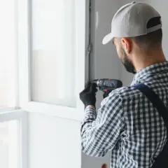 Fachowiec z wiertarką przy oknie. Zastanawiasz się, ile kosztuje naprawa okna?