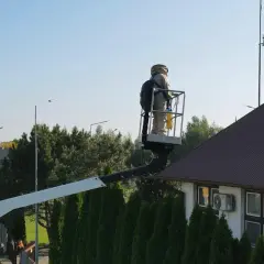 Osoba w stroju pszczelarza na podnośniku koszowym przy dachu domu, przygotowuje się do akcji jak odstraszyć osy z poddasza.