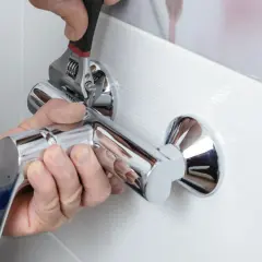Instalacja baterii prysznicowej. Ręce majstra dokręcają chromowaną baterię kluczem nastawnym.