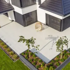 Nowoczesny taras betonowy z wiklinowym fotelem i zielenią. Idealne miejsce na relaks.