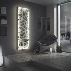 Nowoczesny grzejnik w salonie, ozdobiony ażurowym wzorem i podświetlony, tworzy przytulną atmosferę. Obok fotel i lampa.