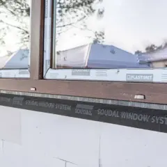Montaż okna w białym pustaku z brązową ramą, widoczna taśma Soudal Window System. Dowiedz się, ile kosztuje montaż okna.