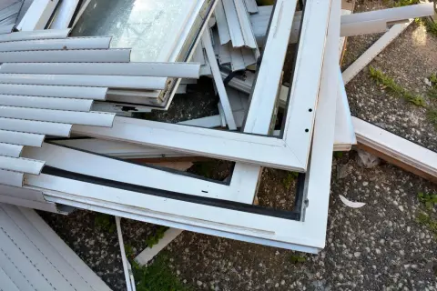 Stare okna PCV czekają na recykling. Widok pokazuje stos białych ram okiennych i szyb, gotowych do przetworzenia.