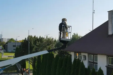 Osoba w stroju pszczelarza na podnośniku koszowym przy dachu domu, przygotowuje się do akcji jak odstraszyć osy z poddasza.