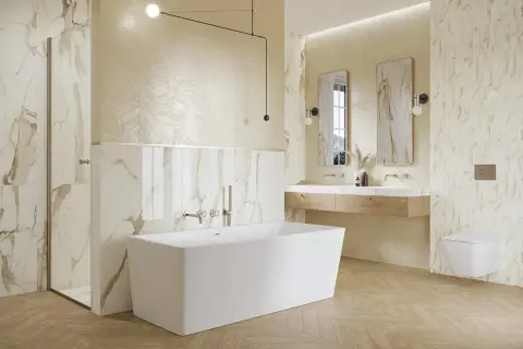 Elegancka łazienka z wanną wolnostojącą, prysznicem i podwójną umywalką. Dominują płytki imitujące marmur z subtelnymi złotymi żyłkami.