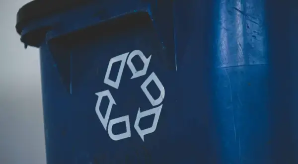 Niebieski śmietnik z symbolem recyklingu. Zastanawiasz się, jak mierzyć odległość śmietnika od okien, by zapewnić komfort i estetykę?