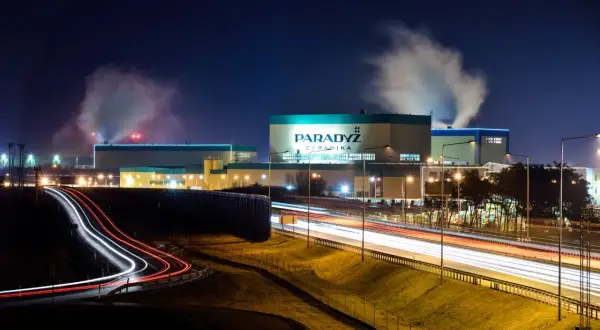 Nocą widać dymiący paradyż zakład produkcyjny w Tomaszowie Mazowieckim. Światła samochodów tworzą smugi na drodze.