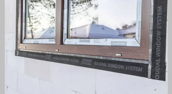 Montaż okna w białym pustaku z brązową ramą, widoczna taśma Soudal Window System. Dowiedz się, ile kosztuje montaż okna.
