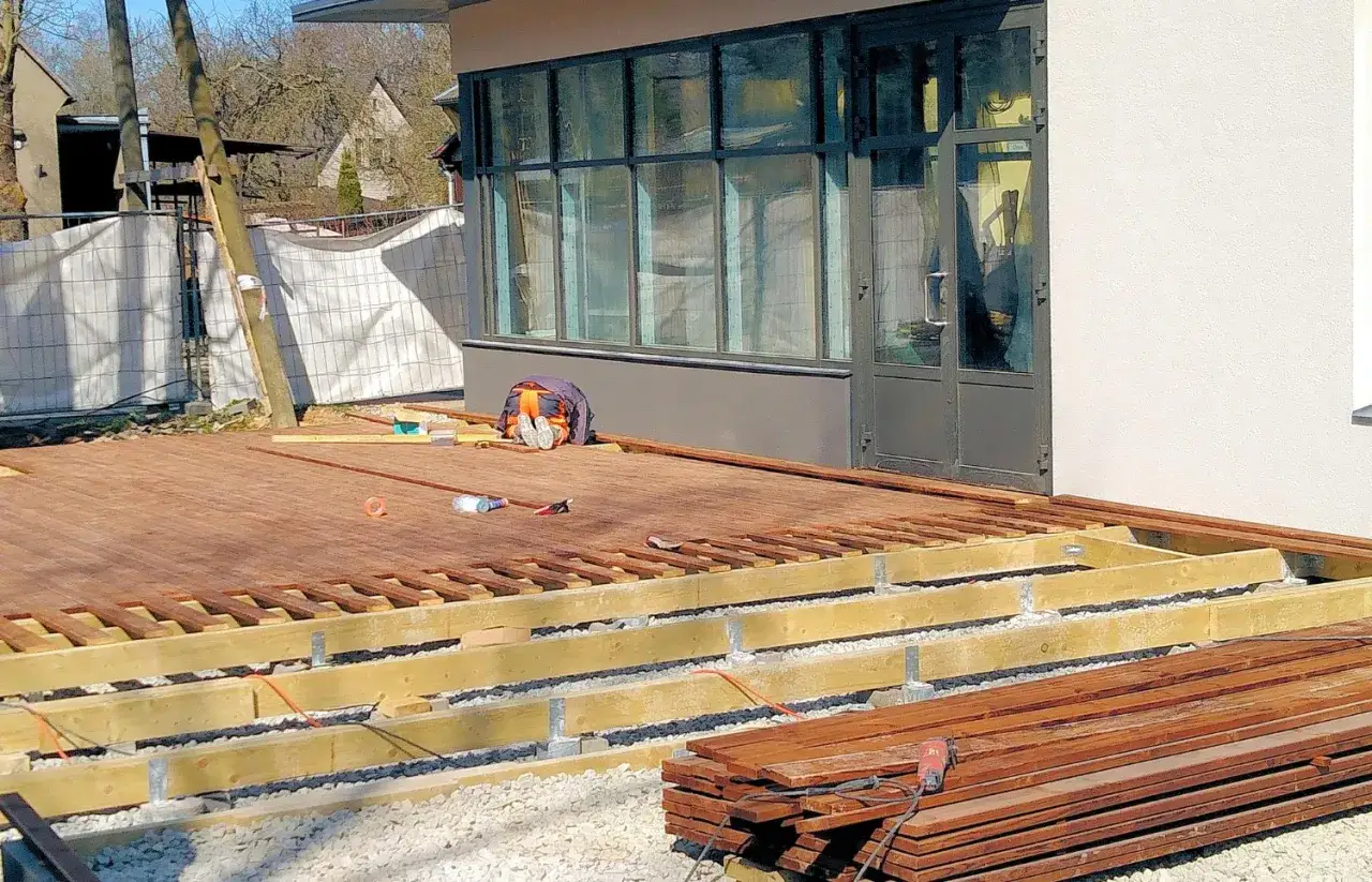 Budowa tarasu z drewna, widać elementy konstrukcyjne i deski. Wkrótce powstanie pergola nad tarasem.