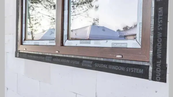 Montaż okna w białym pustaku z brązową ramą, widoczna taśma Soudal Window System. Dowiedz się, ile kosztuje montaż okna.